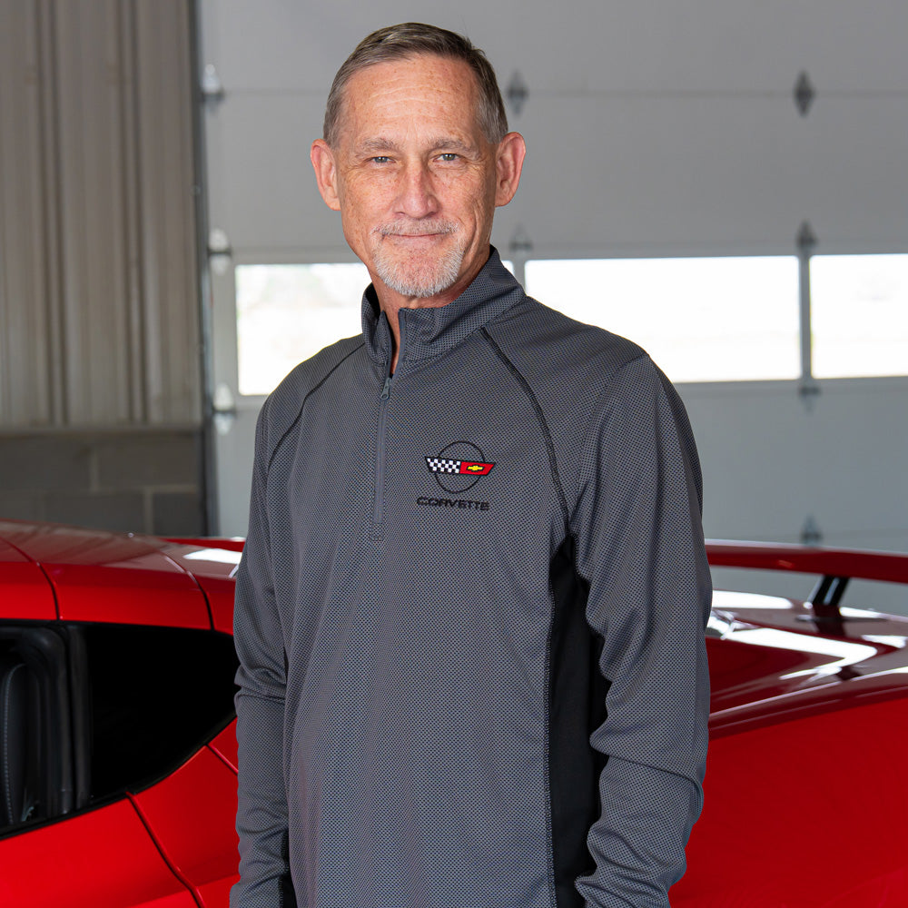 Man wearing the 4th Generation Corvette Emblem Ice Colorblock Quarter-Zip Pullover in Charcoal and black standing in front of a red Corvette