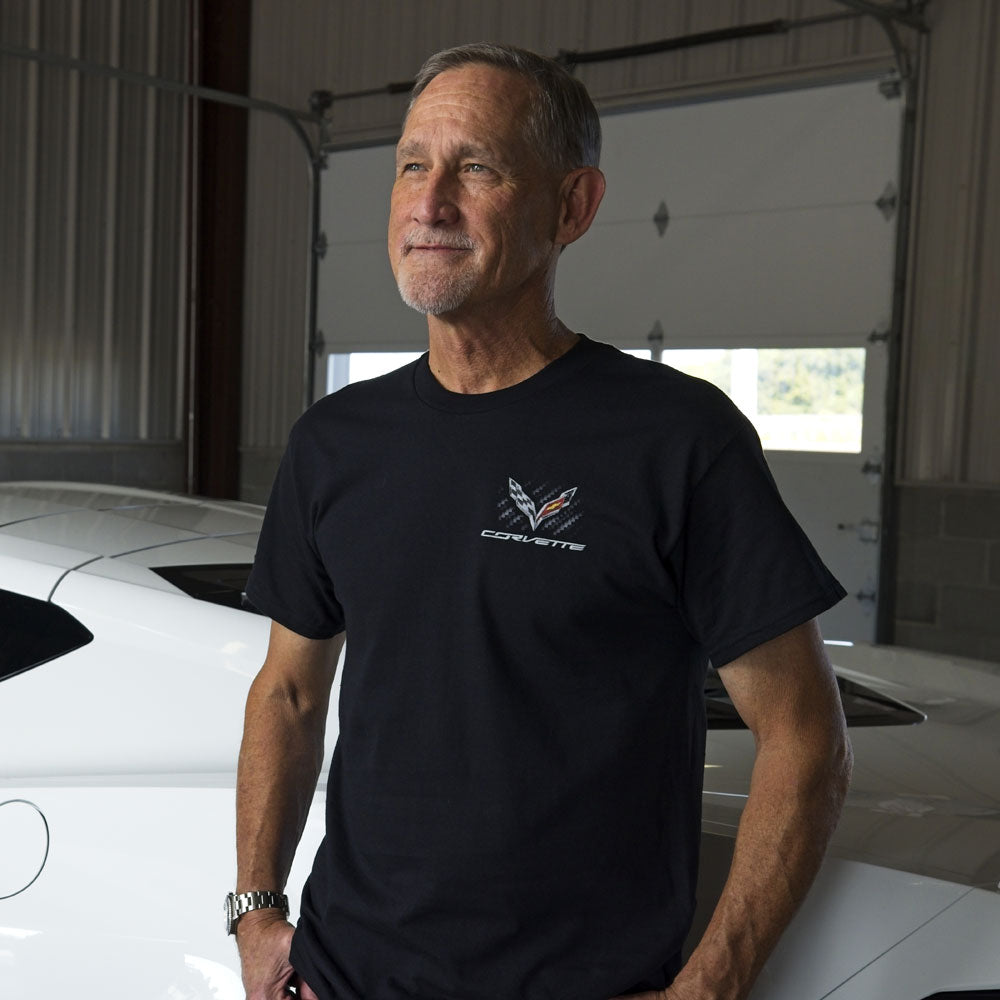 Man standing in a garage wearing a black tee with a C7 Corvette emblem on a carbon fiber background on the front left chest of the tee.