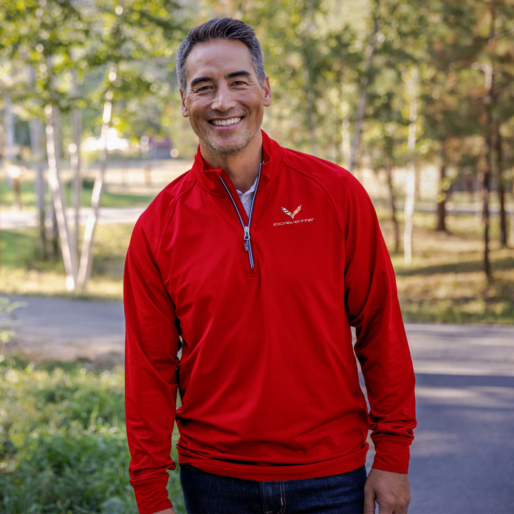 Man wearing a red quarter-zip pullover with a C7 Corvette emblem standing outdoors in a park-like setting.