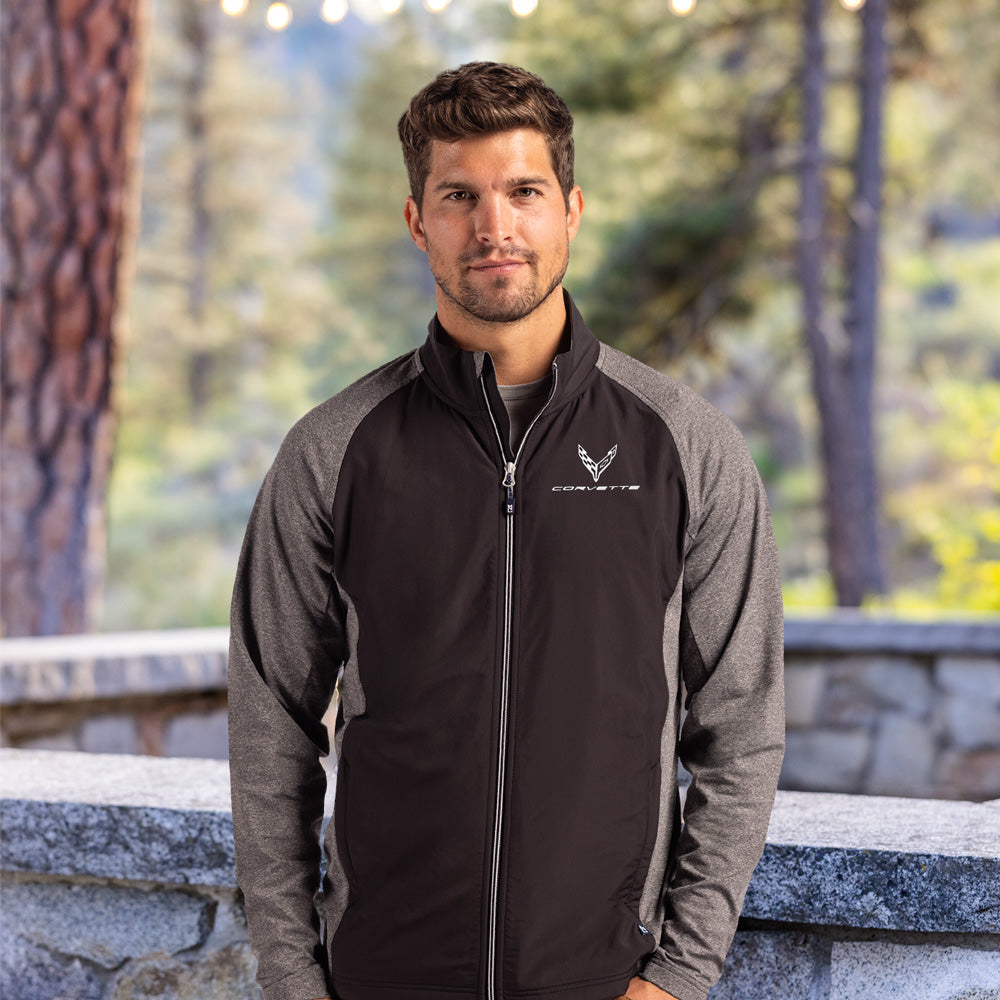 Man wearing a black and gray jacket with a C8 Corvette emblem, standing outdoors with trees in the background