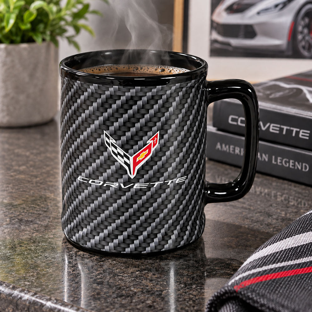 The 8th Generation Corvette Emblem Carbon Fiber Ceramic Mug shown placed on a table in front of some Corvette books.