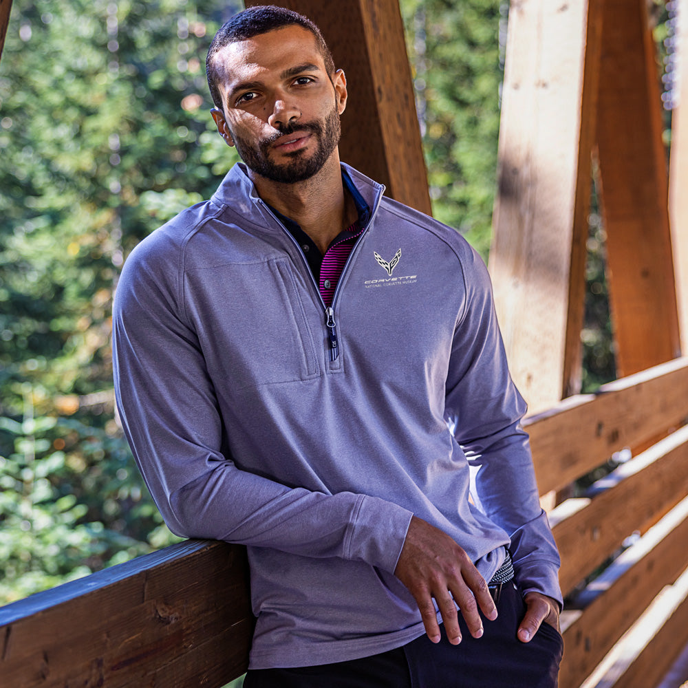 Man wearing a heather navy pullover with a C8 Corvette emblem, standing outdoors near wooden structures and greenery.