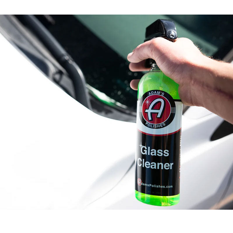 Person spraying Adam's glass cleaner on the windshield of a car