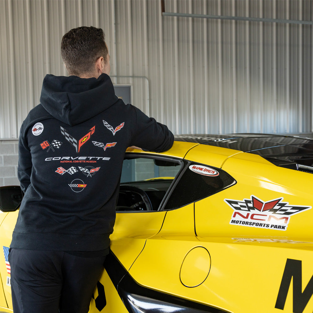Man standing in front of a yellow Corvette showing the back design on the C1-C8 Emblems V-Back Fleece Hoodie
