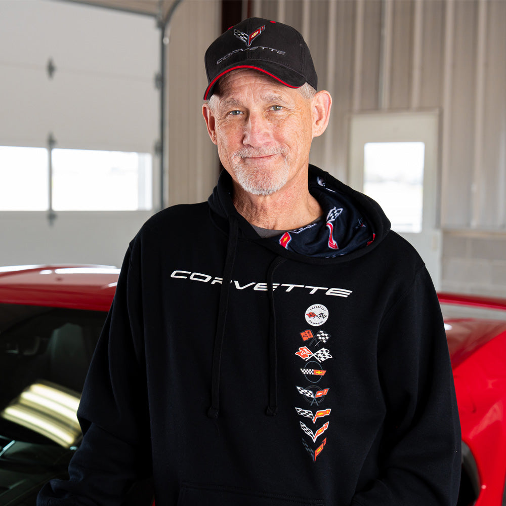 Man wearing a black Corvette hoodie and cap in front of a red Corvette.