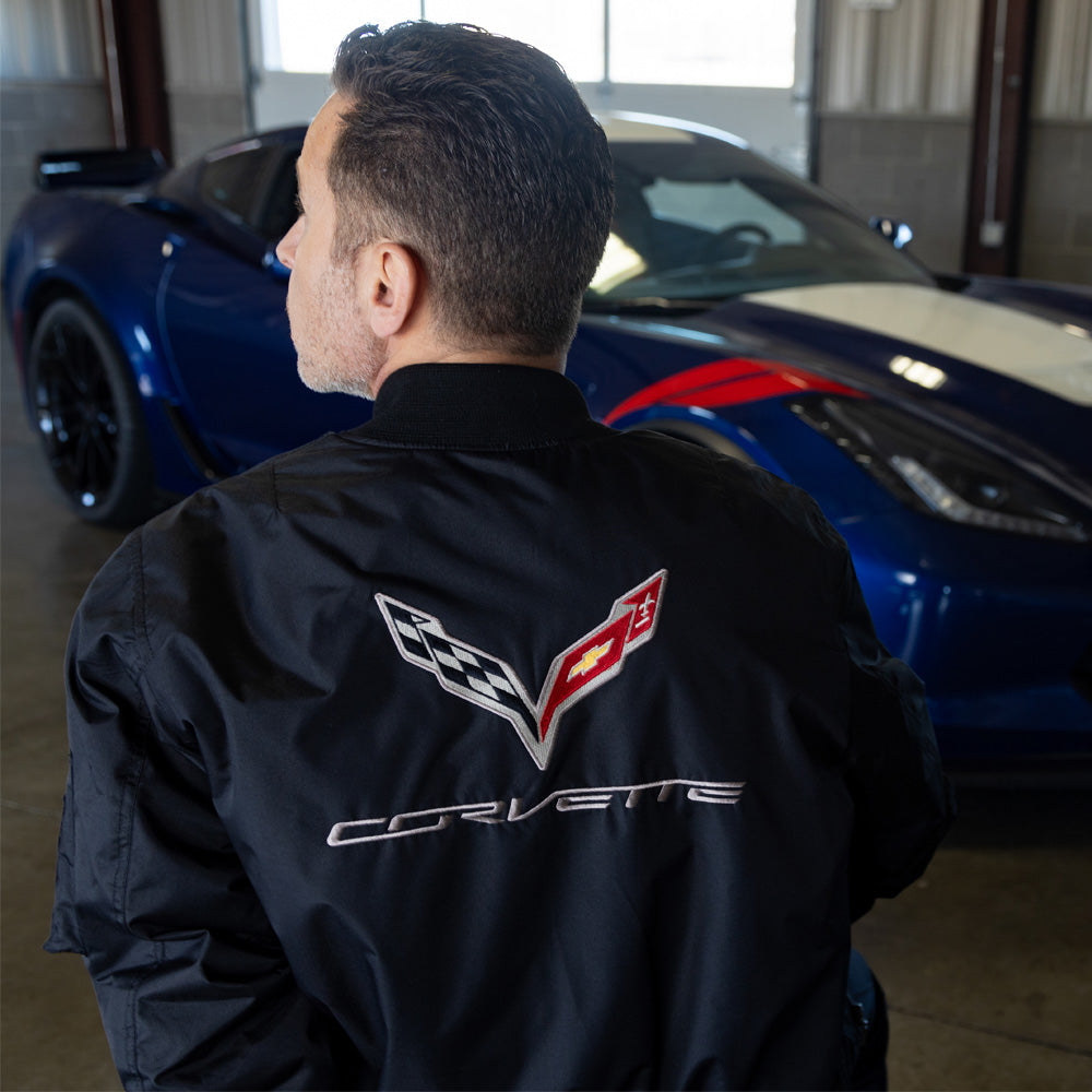 Man seated in front of a C7 Corvette showing the embroidered C7 emblem on the back of the C7 Corvette Aviator Black Jacket