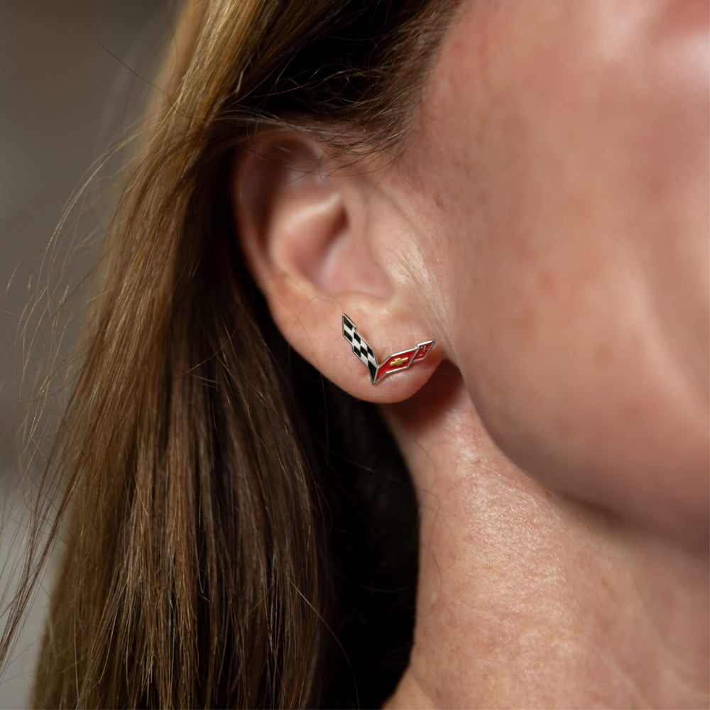 Close-up of an ear wearing a C7 Corvette emblem earring with a blurred background