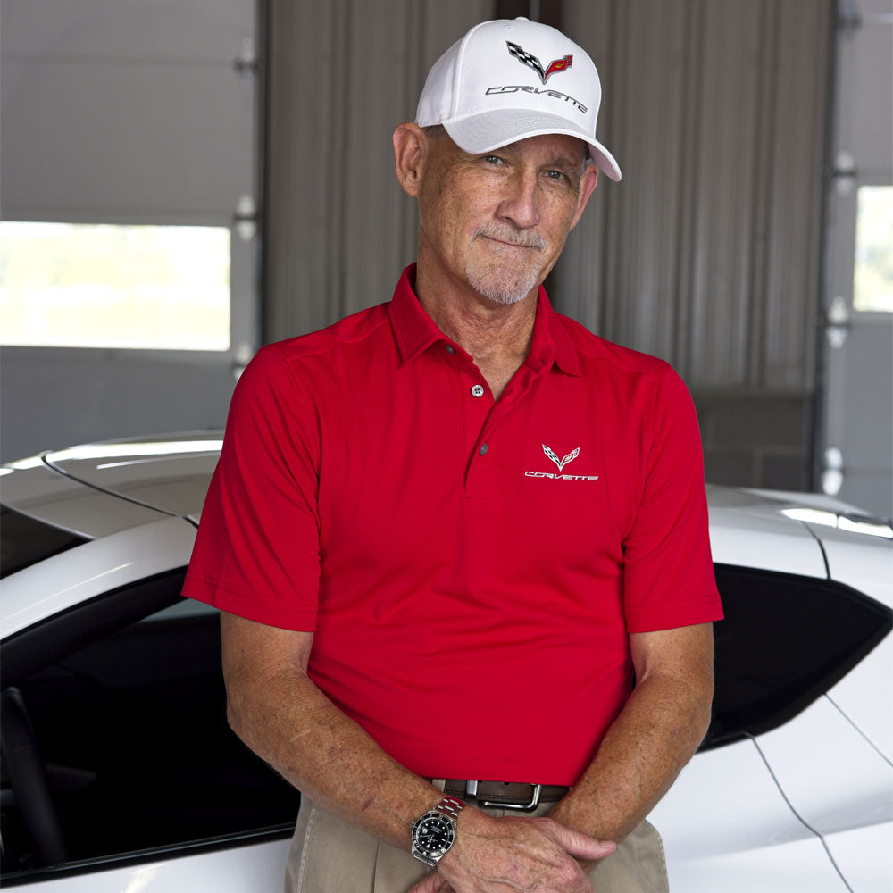 Man standing in front of a white Corvette wearing a red polo with a C7 Corvette emblem embroidered on the left chest.