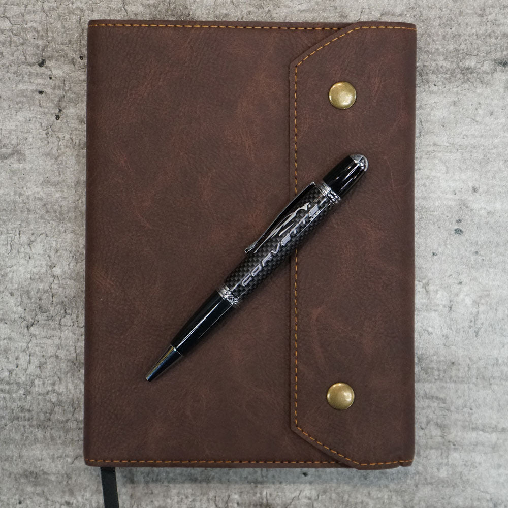 C8 Corvette Gesture Carbon Fiber Material Pen shown on top of a leather padfolio