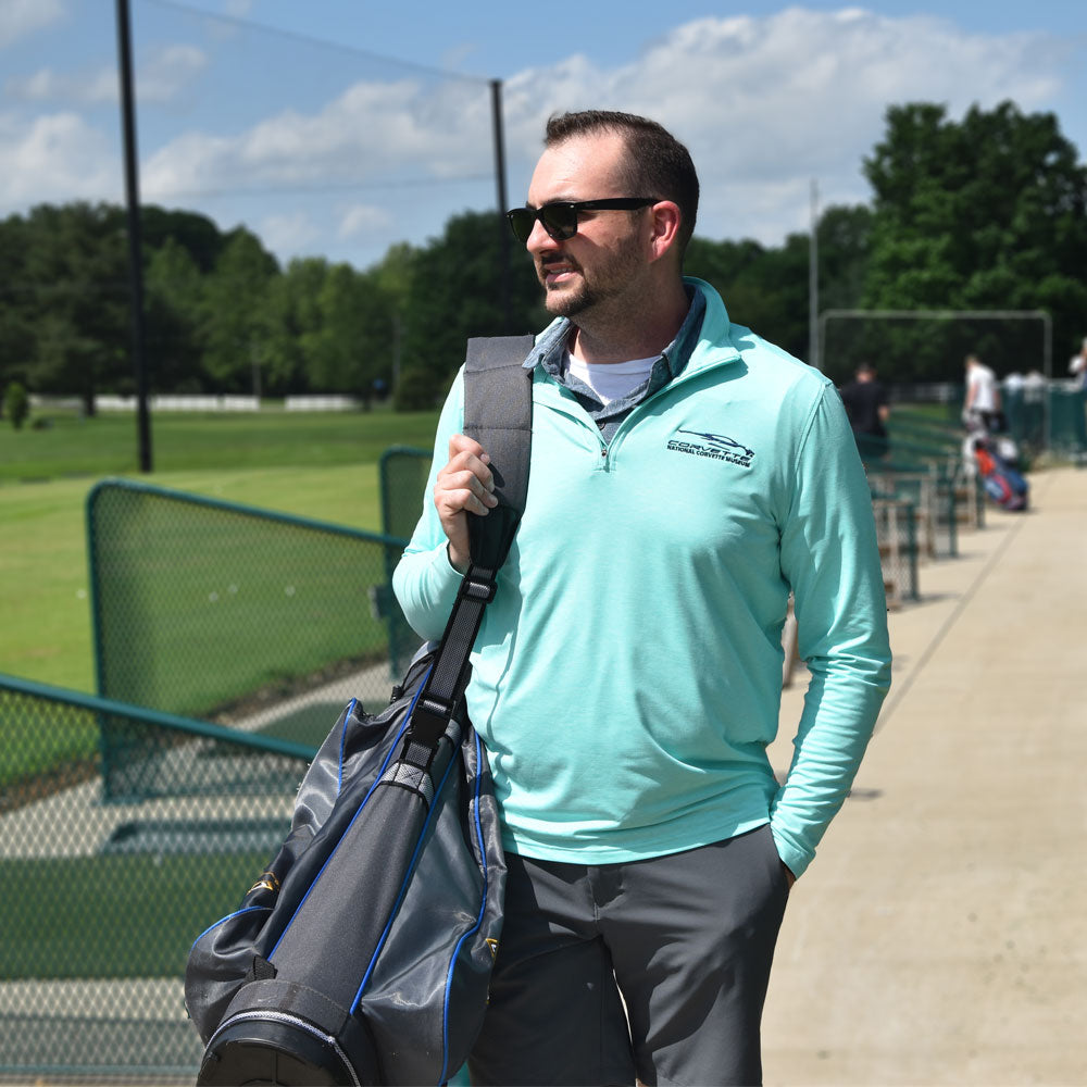 Man wearing the C8 Corvette Gesture Caribbean Green Quarter-Zip Pullover and carrying his golf clubs at the driving range