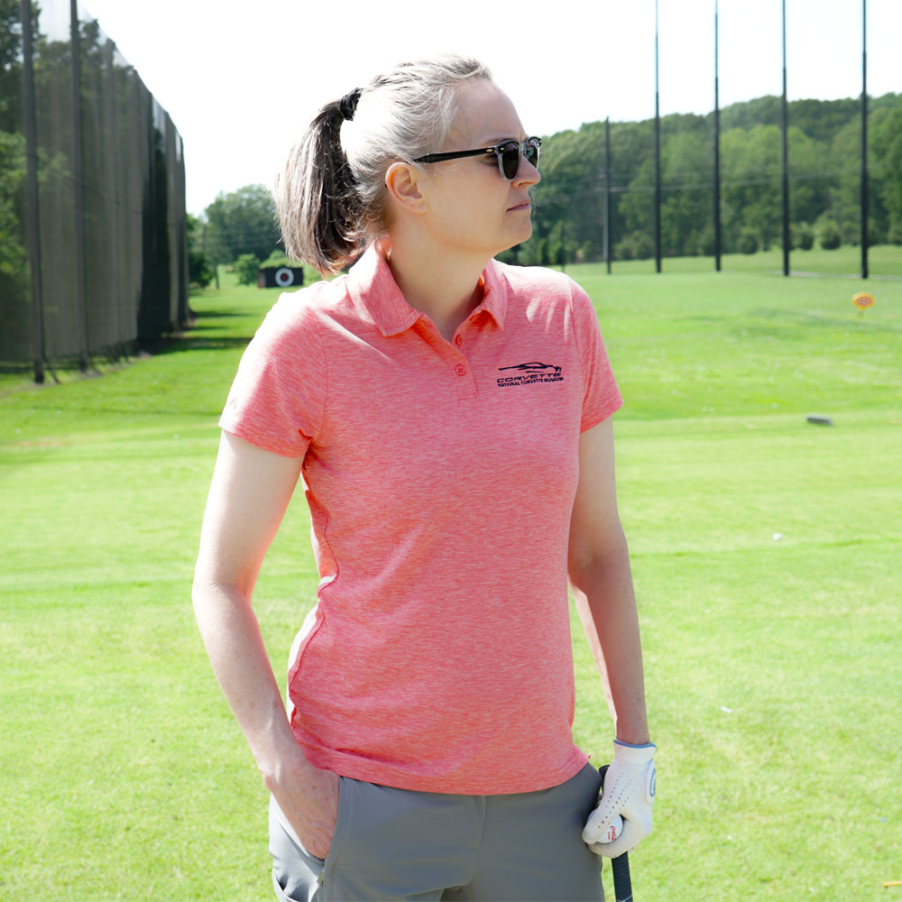 Woman wearing the C8 Corvette Gesture Ladies Heather Coral Matter Polo while shooting golf balls at the driving range