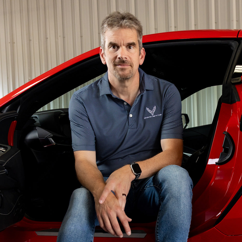 Man sitting in a Red Corvette wearing the C8 Corvette Symmetry Print Stretch Polo