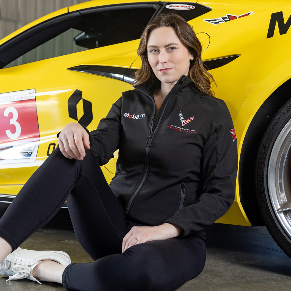 Woman sitting in front of a yellow Corvette wearing the C8R Corvette Racing Mobil 1 Black Jacket