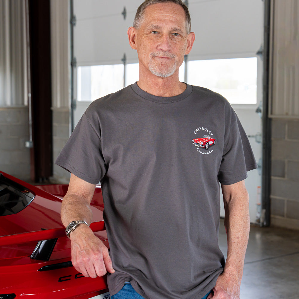 Man wearing a gray t-shirt with a Corvette design on the front left chest, standing in a garage.