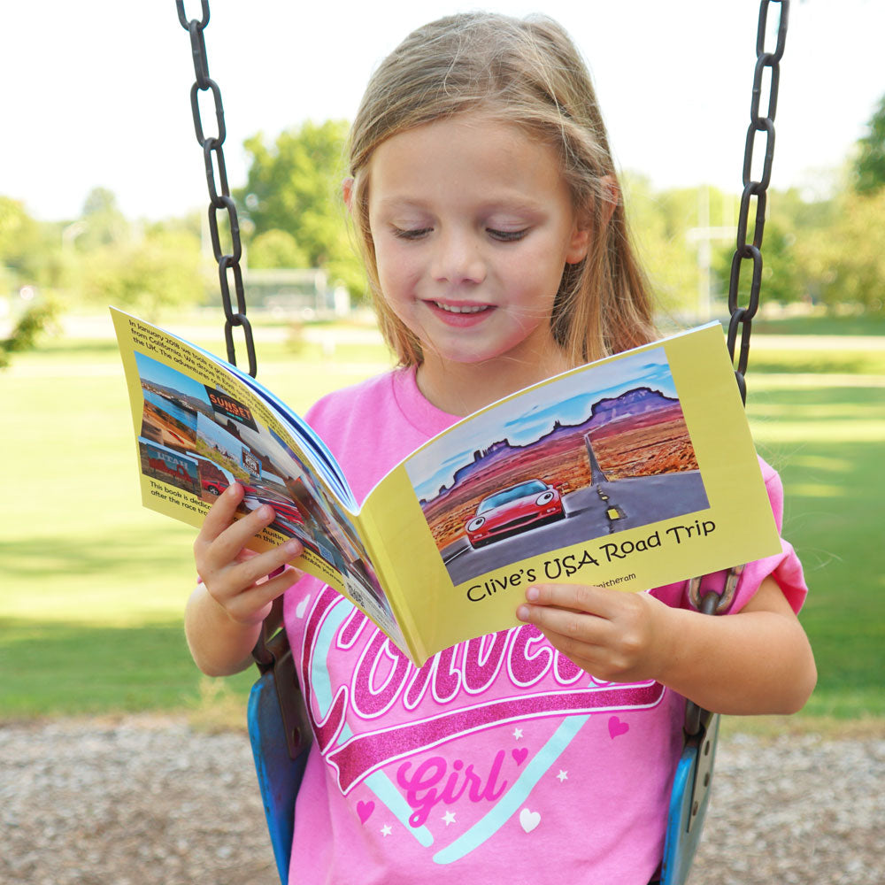 Young girl sitting on a swing reading Clives USA Road Trip book