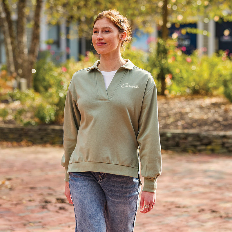 Woman wearing a sage green pullover with Corvette script, standing outdoors.