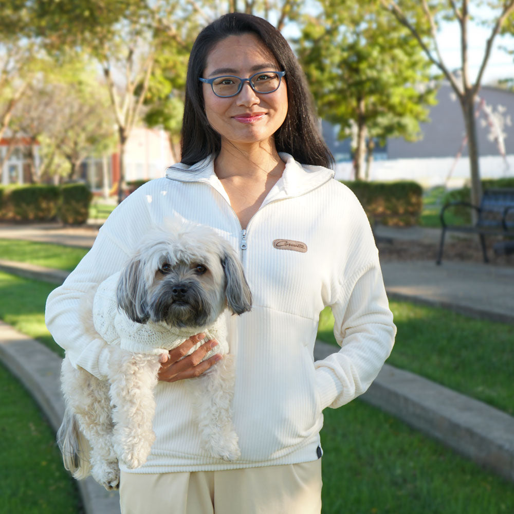 Woman standing in a park holding dog while wearing the Corvette Ladies Corded Half-Zip Vanilla Bean Pullover