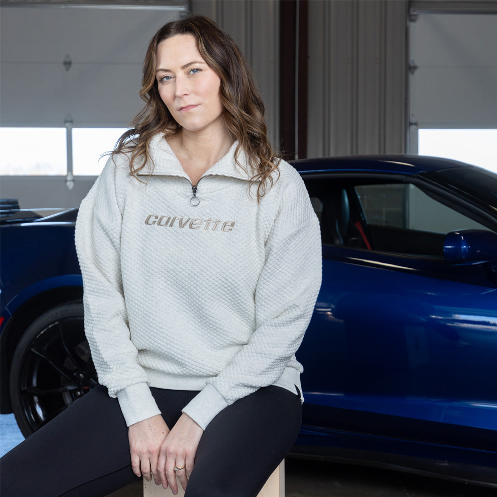 Woman sitting in front of a blue Corvette wearing the Corvette Zip-Collar Quilted Oatmeal Pullover