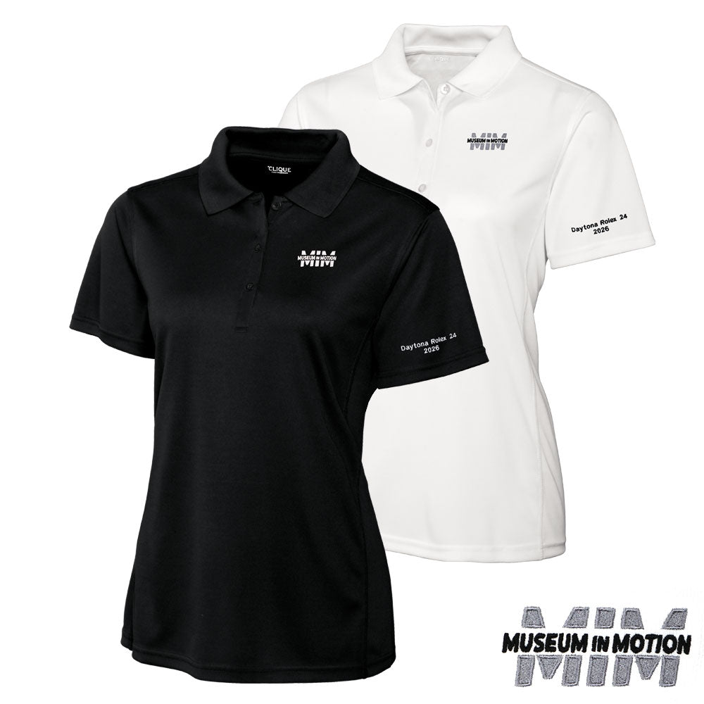 Two women's polo shirts shown on a white background: a black short-sleeve polo in front and a white short-sleeve polo behind it, both with Museum in Motion branding on the chest and tour name on the sleeve.