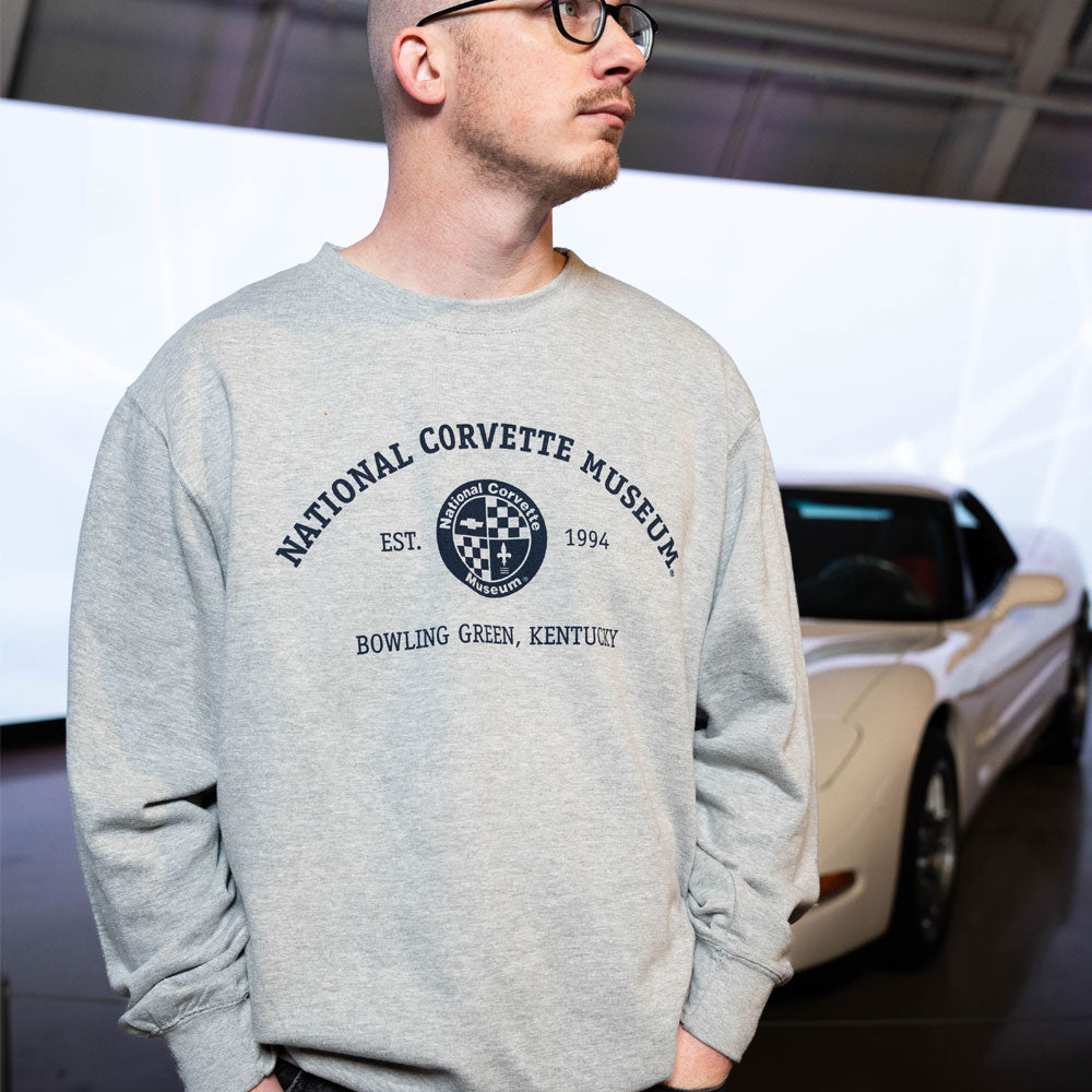 Person wearing the NCM Established 1994 Sweatshirt standing in front of a Corvette 