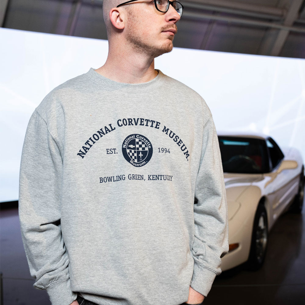 Person wearing the NCM Established 1994 Sweatshirt standing in front of a Corvette