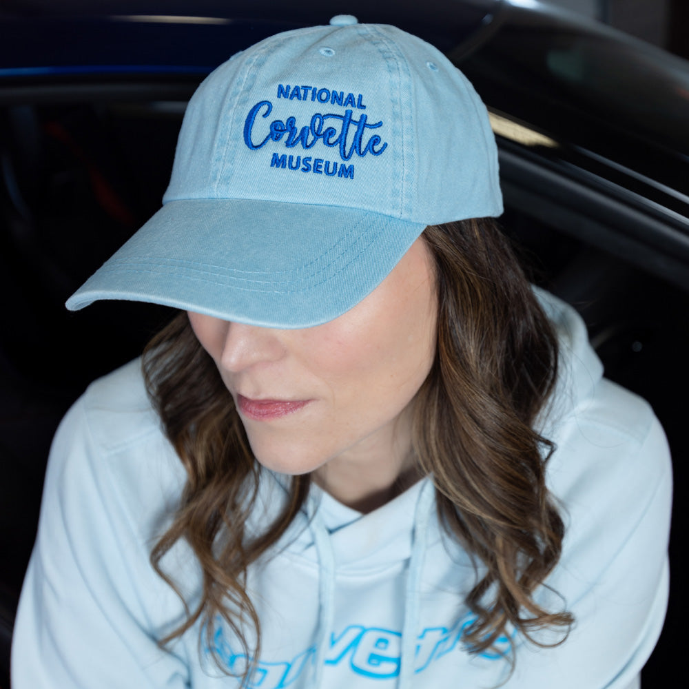 Woman sitting in a Corvette wearing the National Corvette Museum Embroidered Crest Light Blue Cap