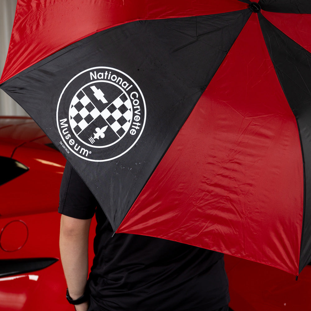 Red and black umbrella with National Corvette Museum logo held by a person in front of a red car.