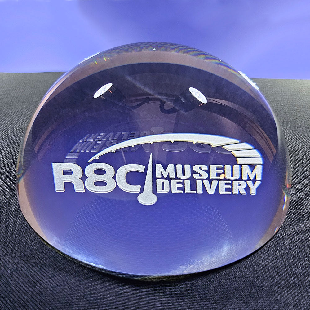 Clear dome paperweight with 'R8C Museum Delivery' text on a blue background