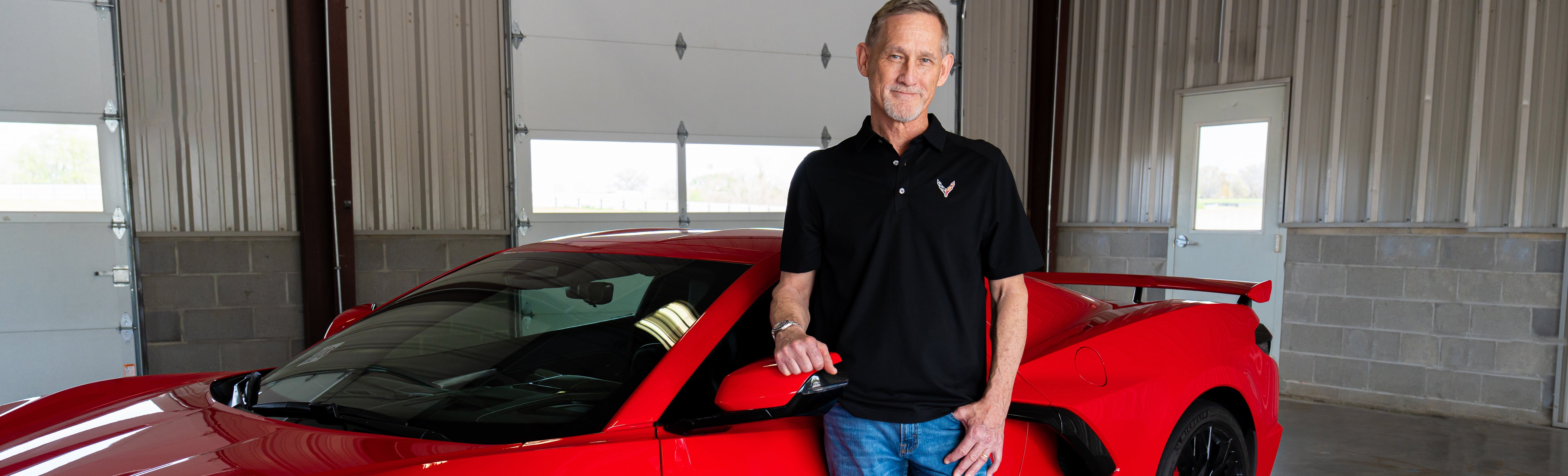 Man standing next to an eighth generation Corvette wearing a black polo with the eighth generation Corvette emblem on the left chest.