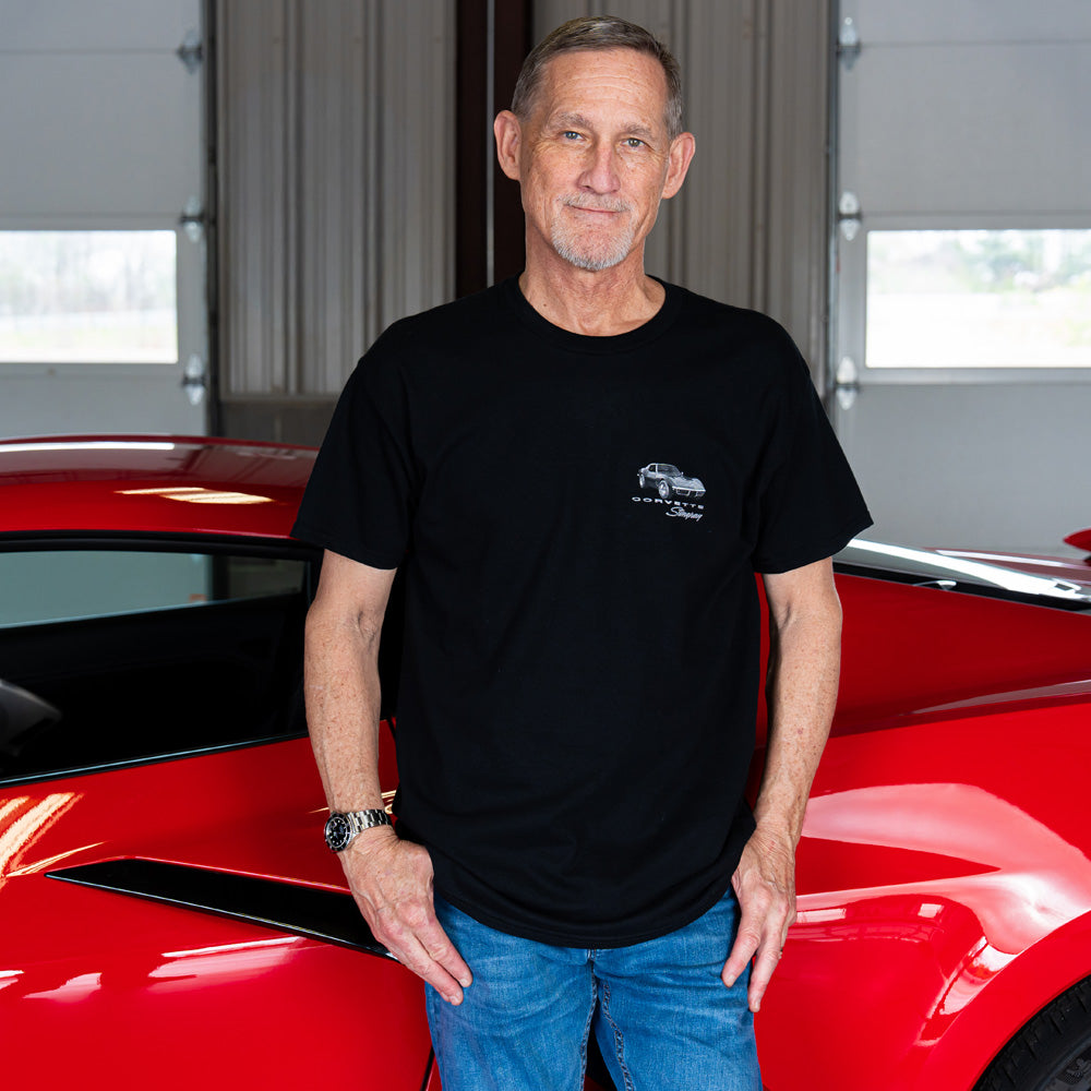 Man standing next to a red Corvette in a garage wearing the 1969 Black Corvette Stingray Black t-shirt.
