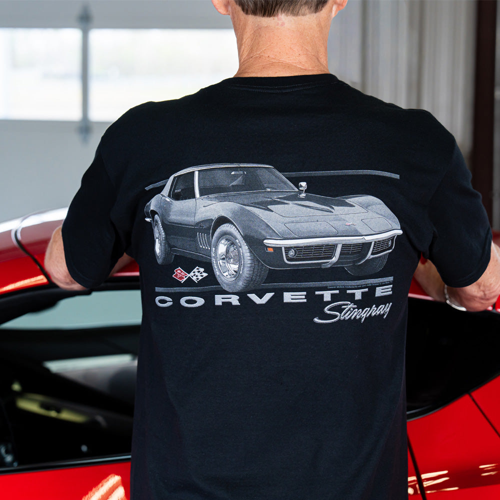 Person wearing a black t-shirt with a Corvette Stingray graphic on the back standing in front of a red Corvette.