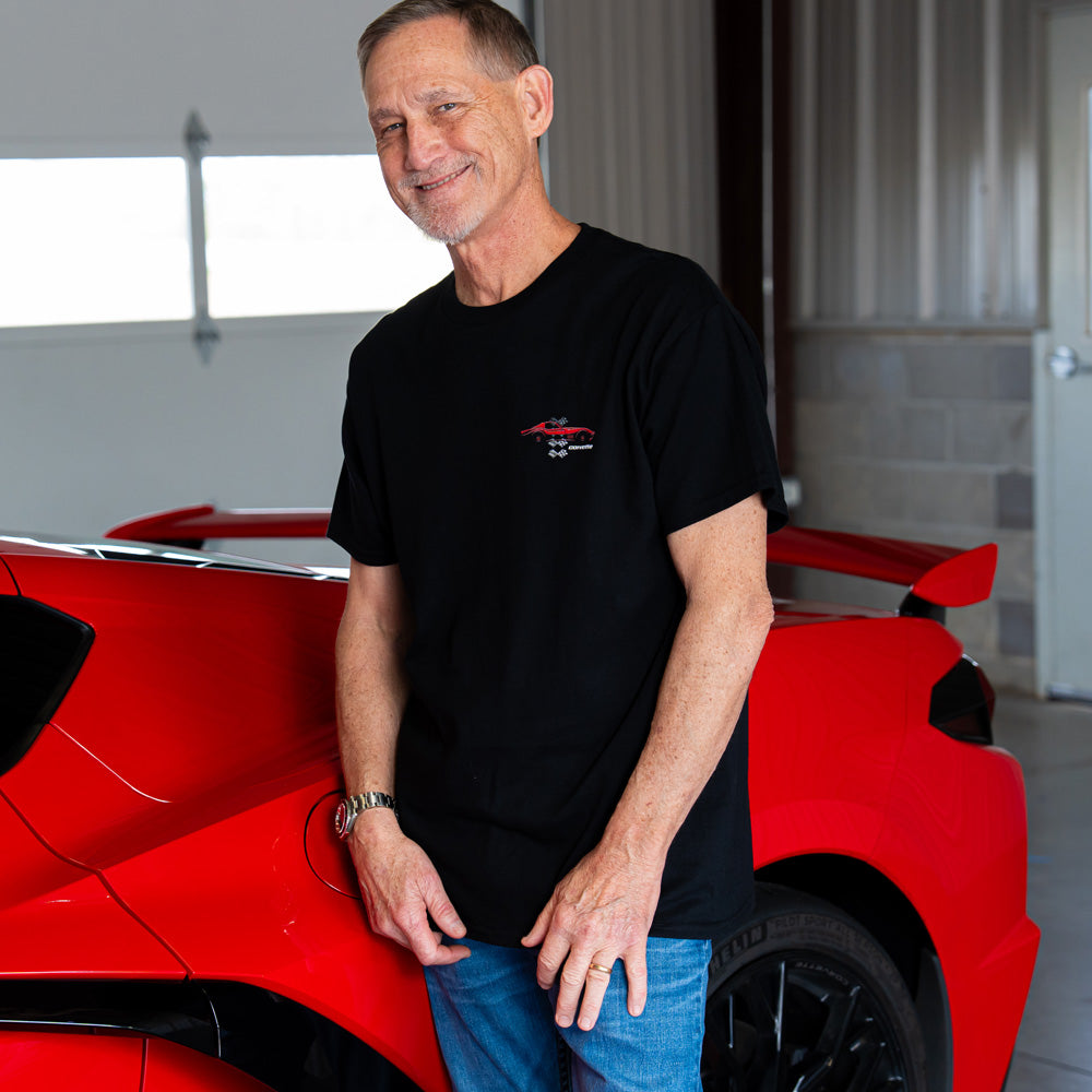 Man standing next to a red Corvette wearing the 1969 Red Vette with Flags black T-shirt 