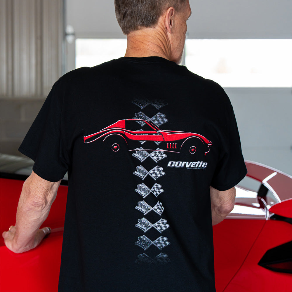Person wearing a black t-shirt with a Corvette design, standing in front of a red Corvette.