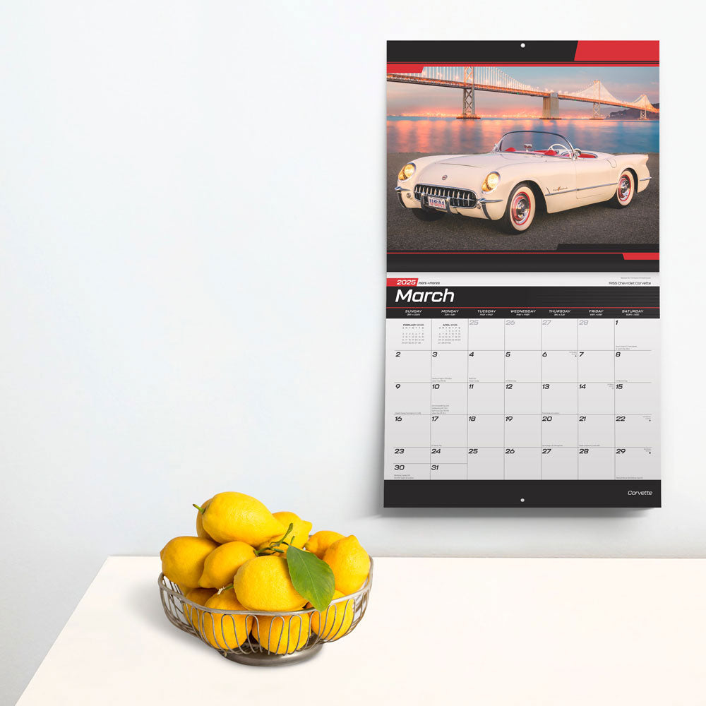 2025 Deluxe Corvette Wall Calendar shown hanging on the wall next to a bowl of lemons