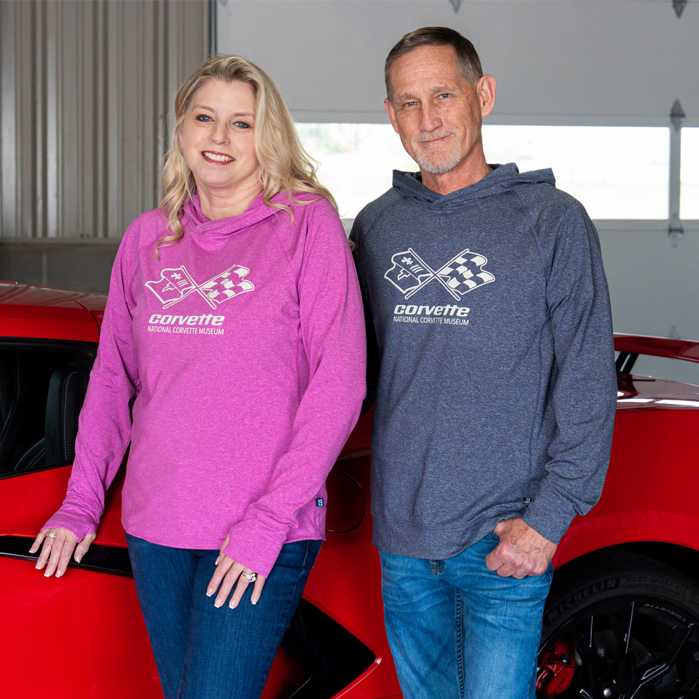 Two people wearing Corvette hoodies with the C3 Corvette emblem on the front standing in front of a red car.