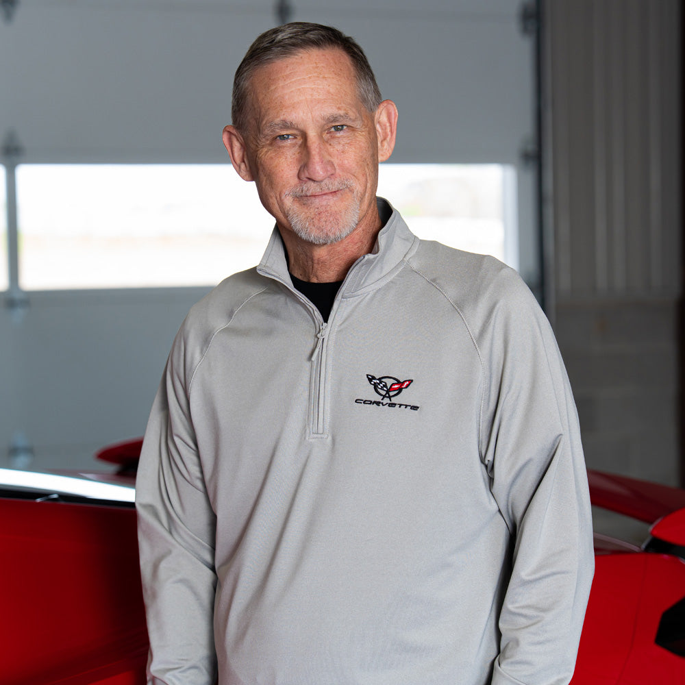 Man wearing the 5th Generation Corvette Emblem Dash Quarter-Zip Pullover in gray standing in front of a red Corvette.