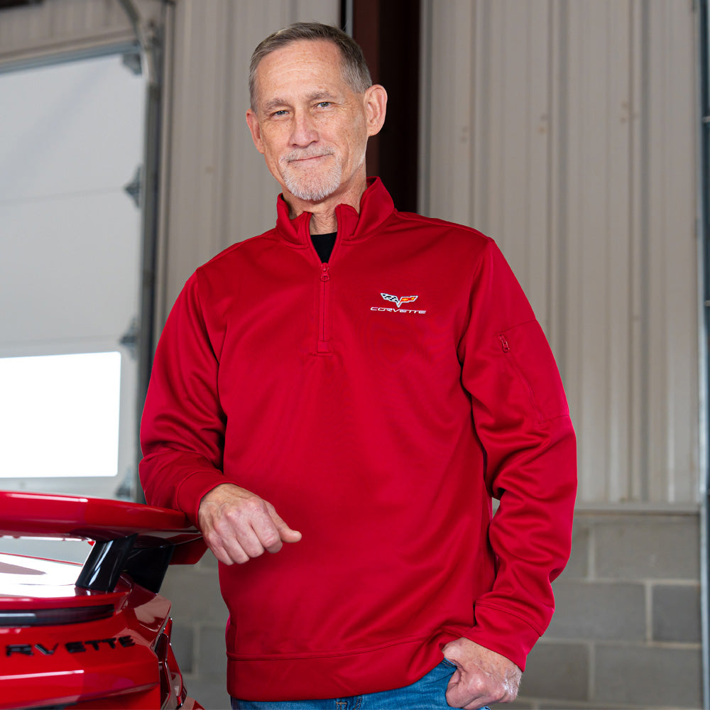 Man standing in a garage next to a red Corvette wearing the 6th Generation Corvette Emblem Lift Red Quarter-Zip Pullover