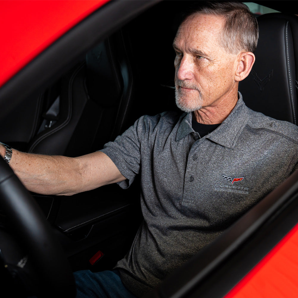 Man sitting inside a red Corvette wearing a heather black polo with a C6 Corvette emblem.