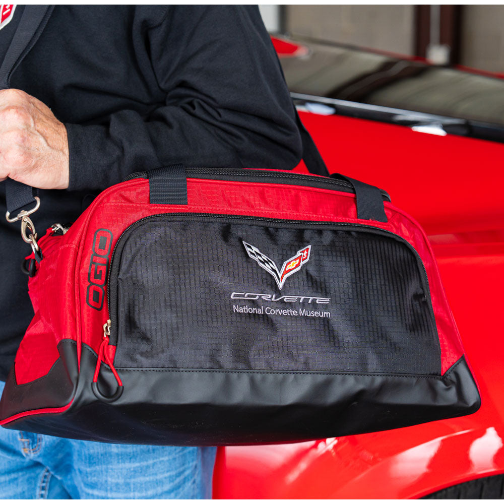 A person carrying the 7th Generation Corvette Duffle Bag standing in front of a red Corvette.