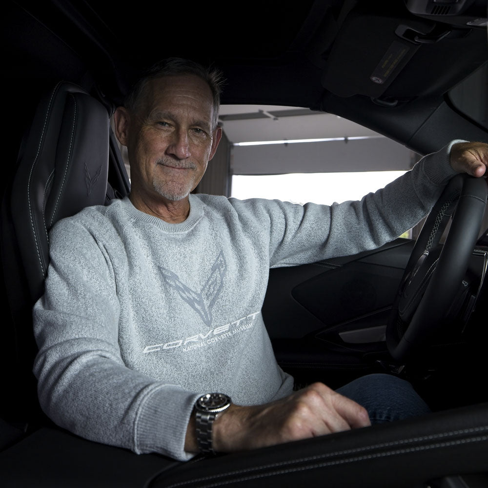 Man sitting in the driver seat of a Corvette wearing the 8th Generation Corvette Emblem Crewneck Pullover in Light Steel