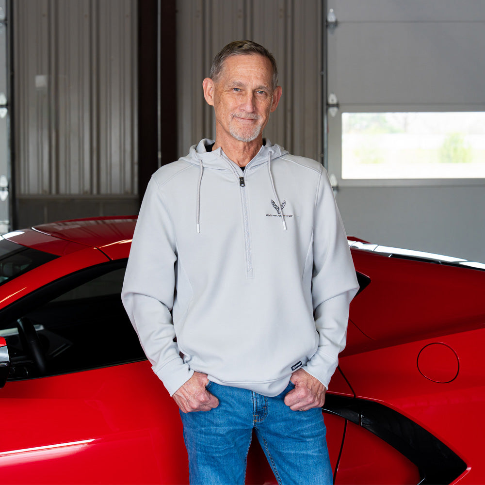Man wearing the 8th Generation Corvette Emblem Roam Half-Zip Pullover standing next to a  red Corvette  in a garage.