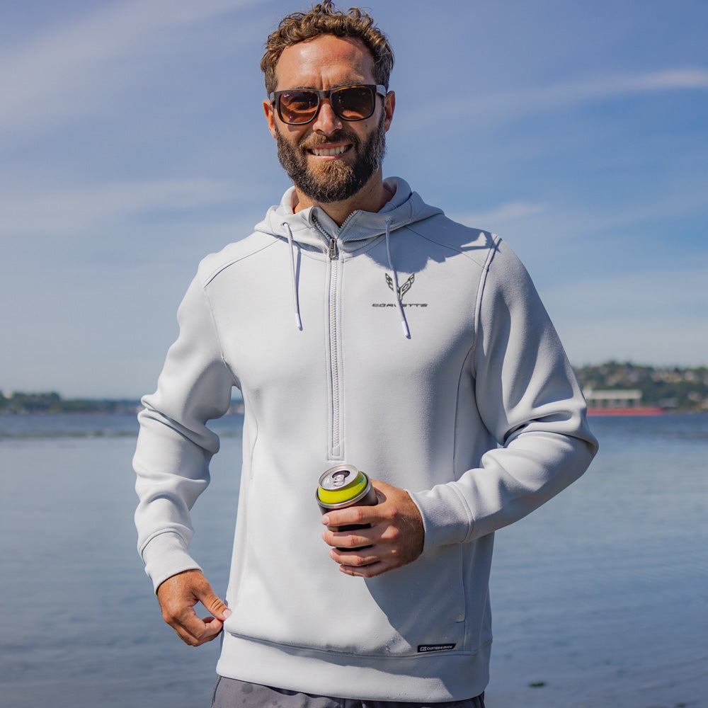 Man wearing a light gray half-zip hoodie embroidered with the C8 Corvette emblem on the left chest while standing by a body of water