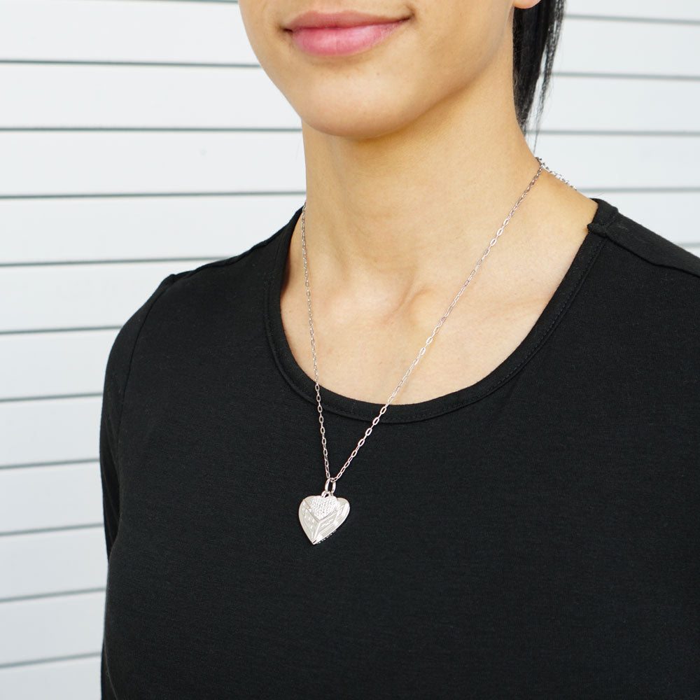 Person wearing a silver heart-shaped C8 Corvette emblem pendant necklace against a neutral background