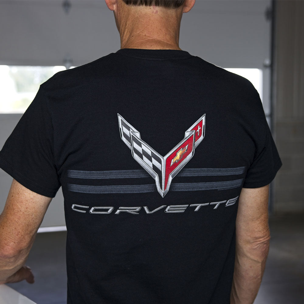 Man standing in a garage wearing the black t-shirt with a large C8 Corvette emblem design over two horizontal tire tracks.