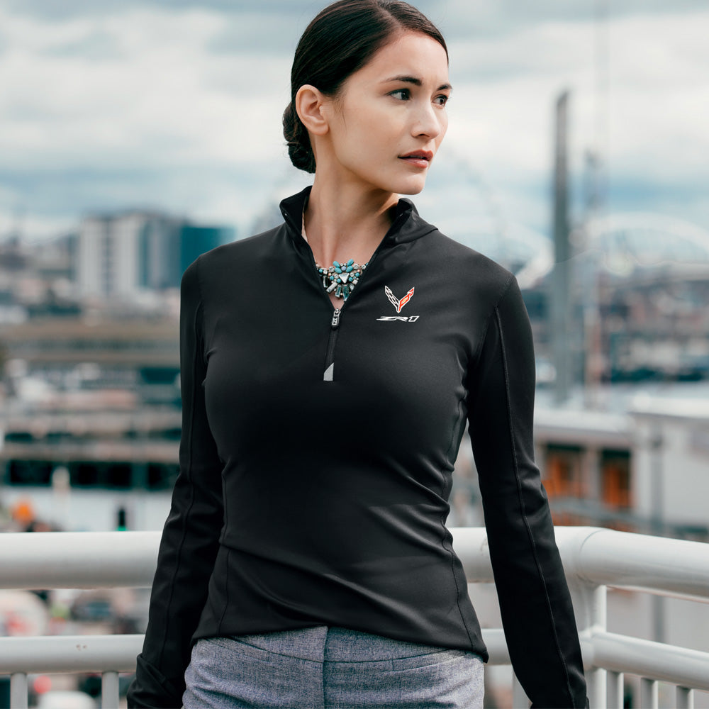Woman wearing a black quarter zip pullover with a C8 ZR1 Corvette logo, standing on a bridge with a cityscape background
