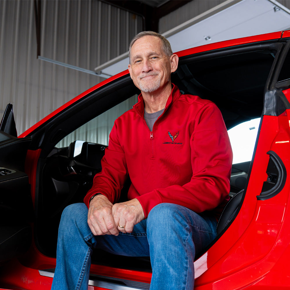 Man sitting in a red Corvette wearing the 8th Generation Z06 Corvette Emblem Lift Red Quarter-Zip Pullover