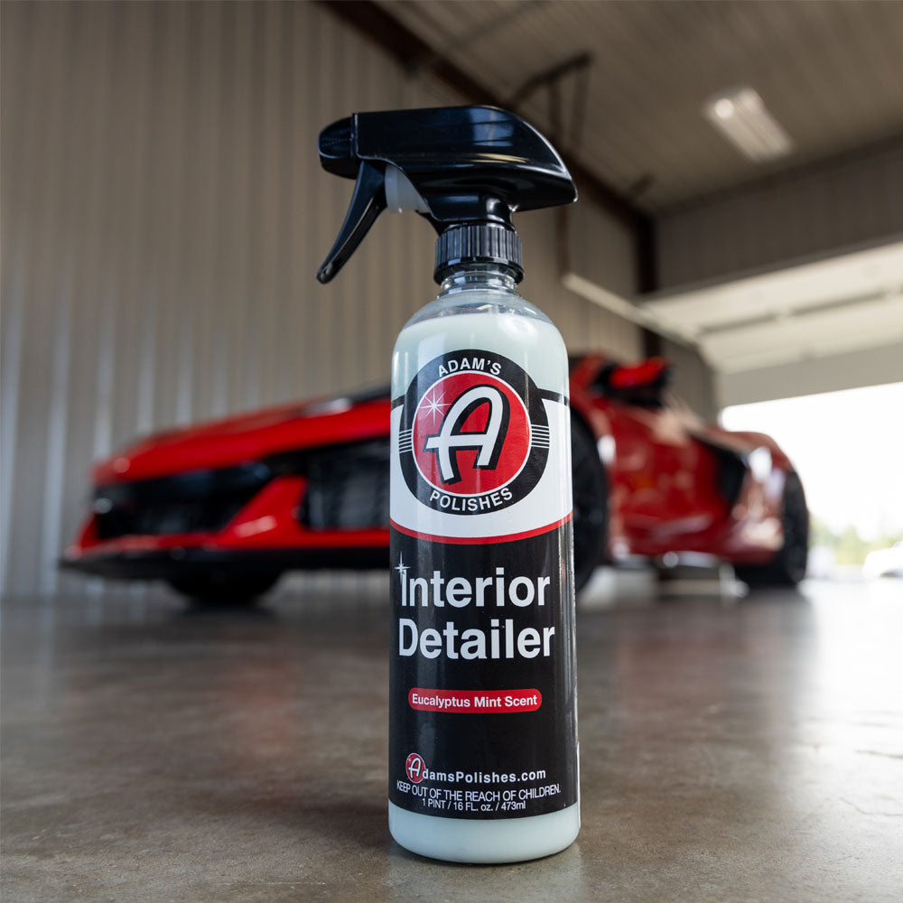 Adams Total Interior Detailer placed on a garage floor in front of a red Corvette