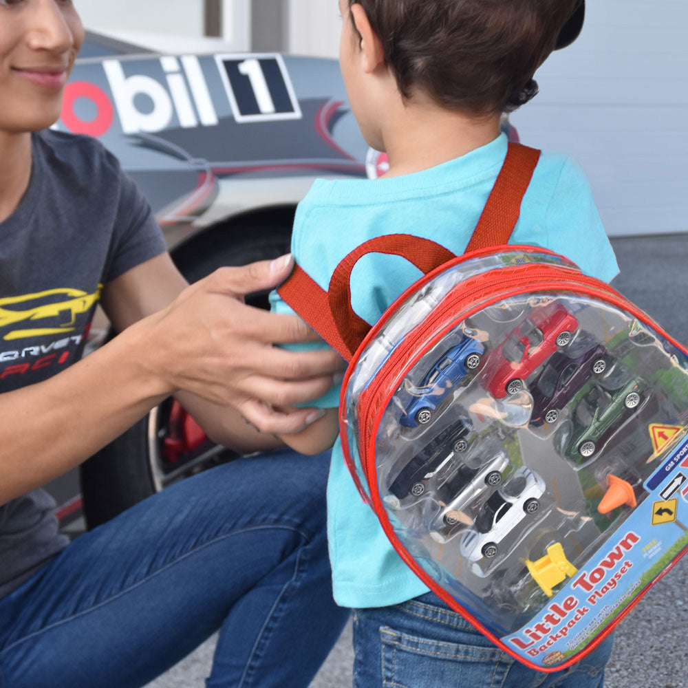 Child with a backpack full of toy Corvettes standing in front of a Corvette.