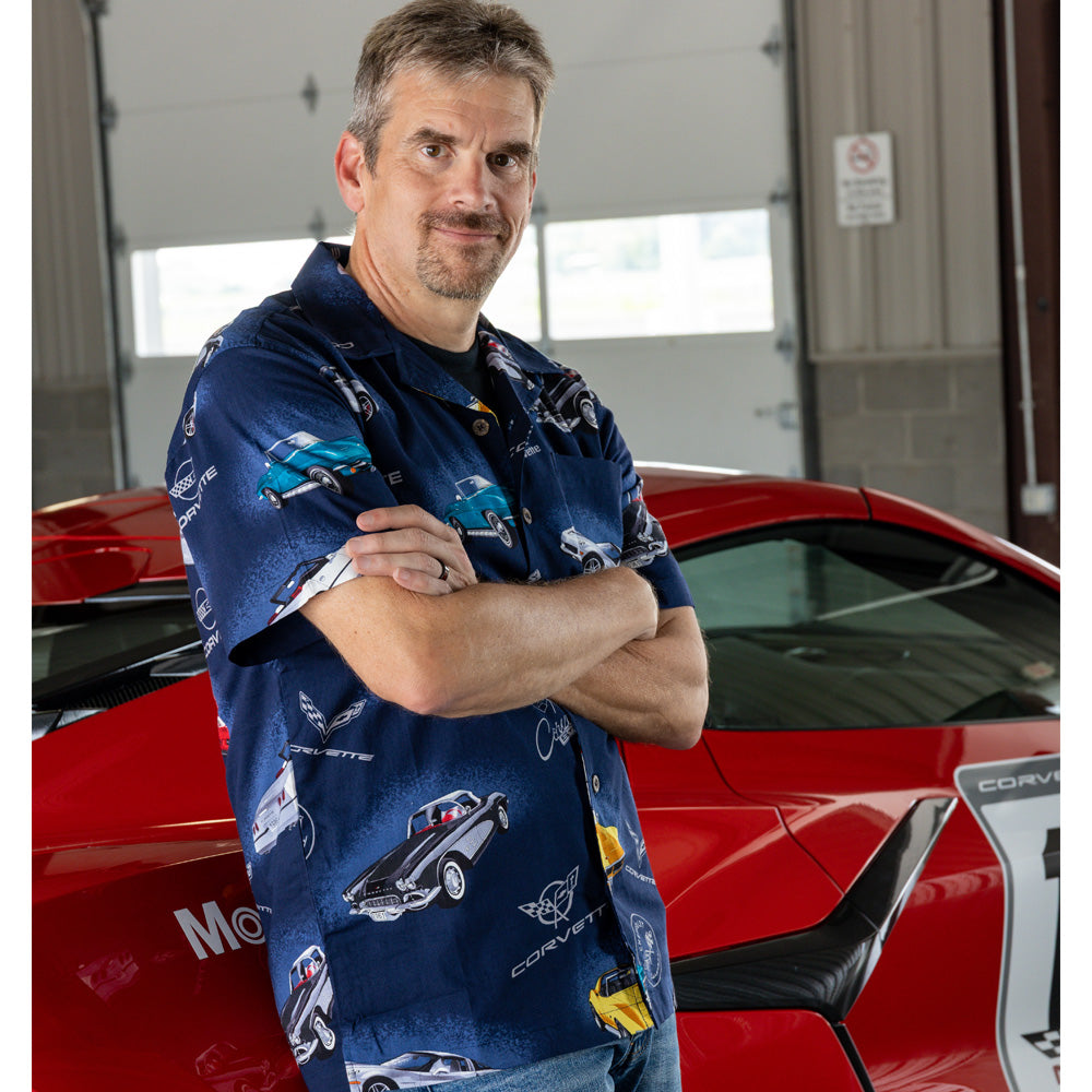 Man standing in front of a red Corvette wearing a Navy camp shirt with a Corvette pattern.