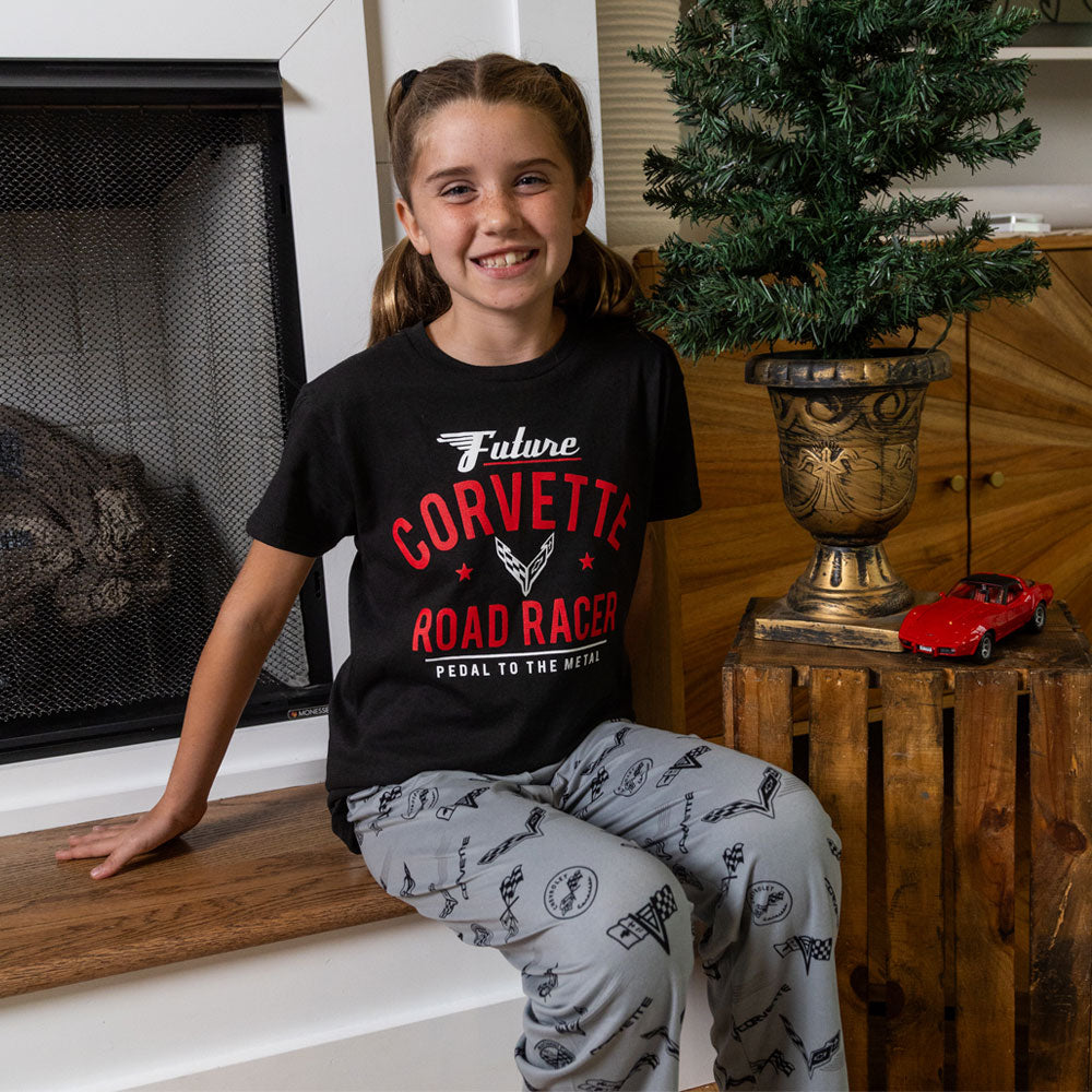 Youth sitting by a fireplace wearing the C1 through C8 Corvette Emblems Print Youth Lounge Pant